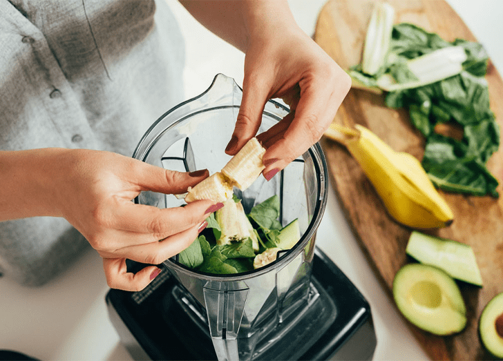 Woman is preparing a green smoothie with fresh fruits, green spinach and avocado.
