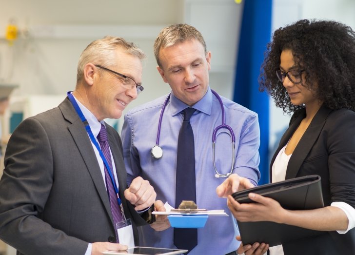 Three health care leaders standing in a hallway looking at an iPad.