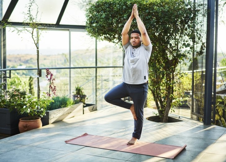 Man practices yoga and standing balance on a mat. 