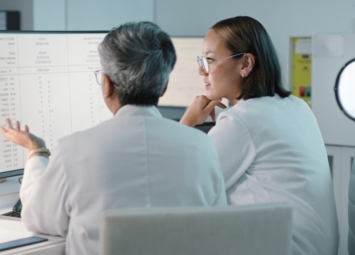 Two clinician scientists sit at a computer looking at data. 