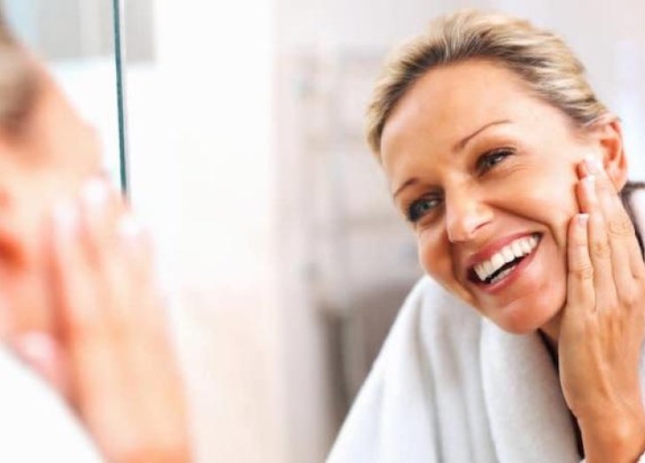 Woman touches her face while looking in the mirror. 