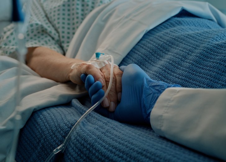doctor holding elderly hand in hospital bed.